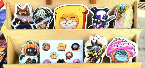 Photograph of Mastafran's table at Alley Art Fest 2026 in Aurora,IL. This picture showcases his selection of stickers.